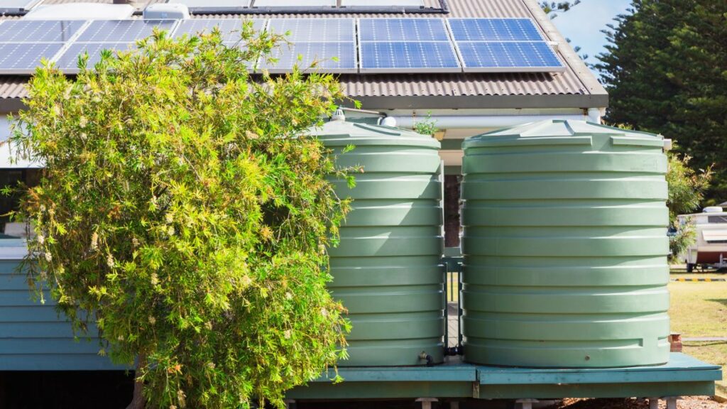 Twee groene wateropslagvaten staan bij een huis met zonnepanelen op het dak