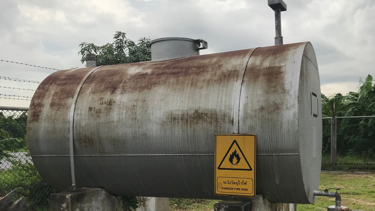 Een oude, verroeste mazouttank in een tuin met prikkeldraad.