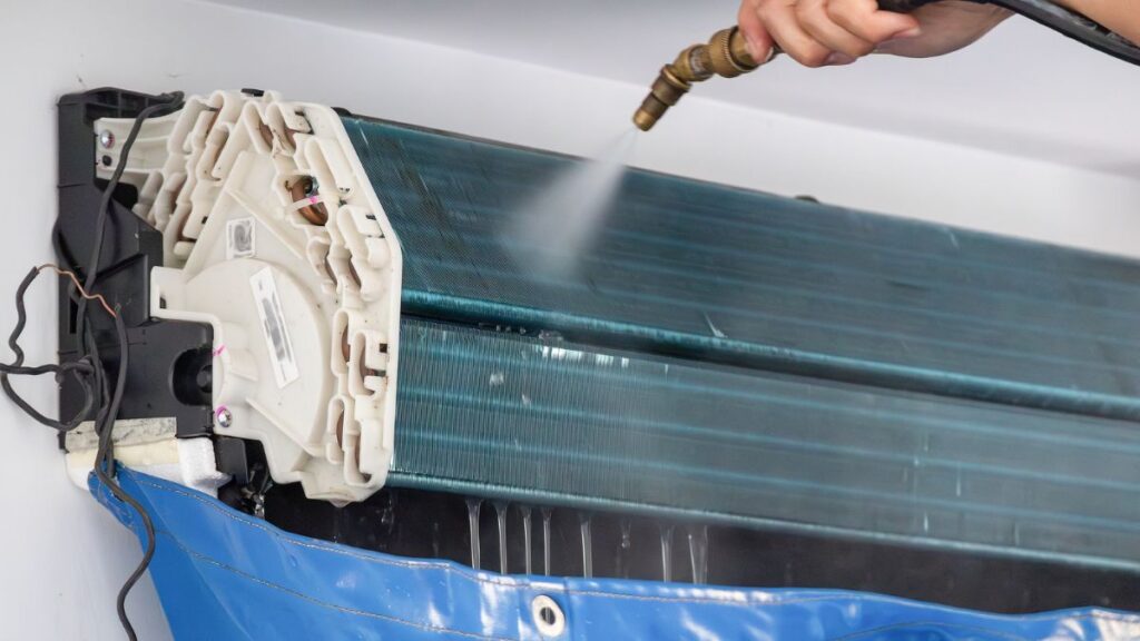 Een technicus die een airco aan het reinigen is met een hogedrukreiniger voor het verwijderen van vuil uit de binnenunit.