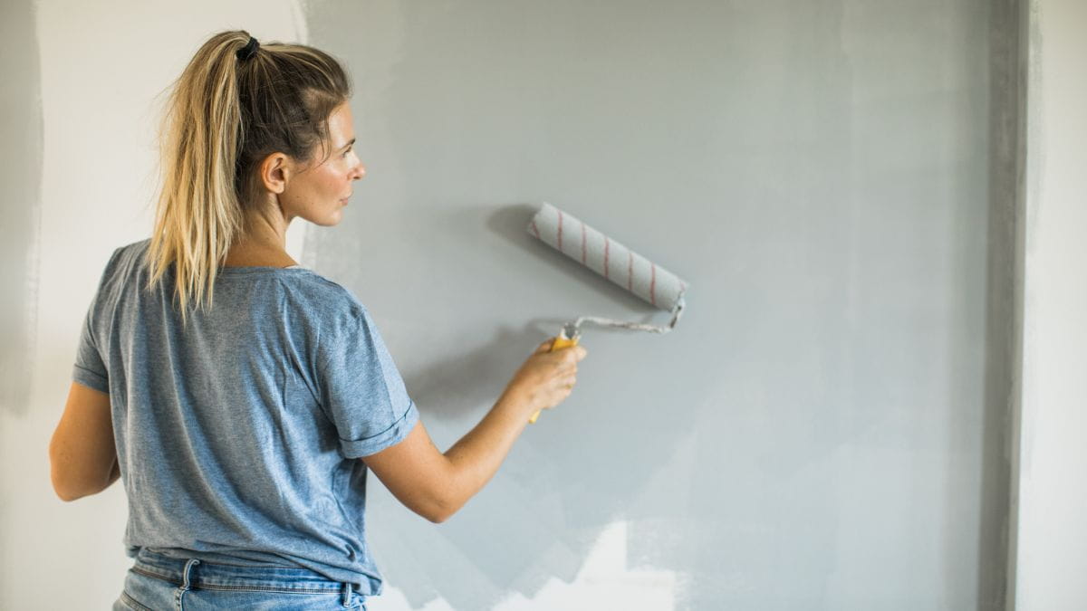 Vrouw schildert muur in grijs met een verfroller 