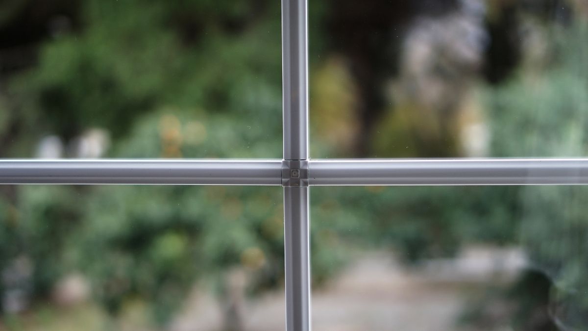 Detailbeeld van witte kruishouten in een raam dat uitgeeft op een groene tuin.