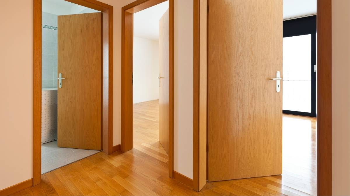 Drie tubespaan deuren met fineerhouten toplaag. Alle drie de deuren zijn geopend. De meest linkse deur geeft uit op een badkamer. De middelste deur leidt naar een kamer met parket en witte muren. De rechtse deur geeft uit op een ruimte met parket en een groot raam met zwarte kozijnen. 
