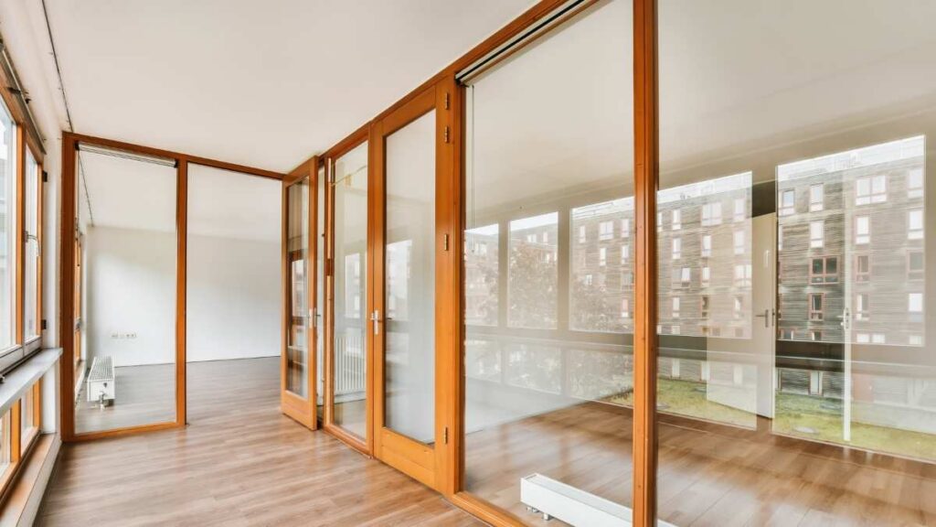 Een verdieping met een glazen wand in houten kozijnen en een parketvloer. Achterin de ruimte zit een plafondhoge glazen deur met hetzelfde houten kozijn.