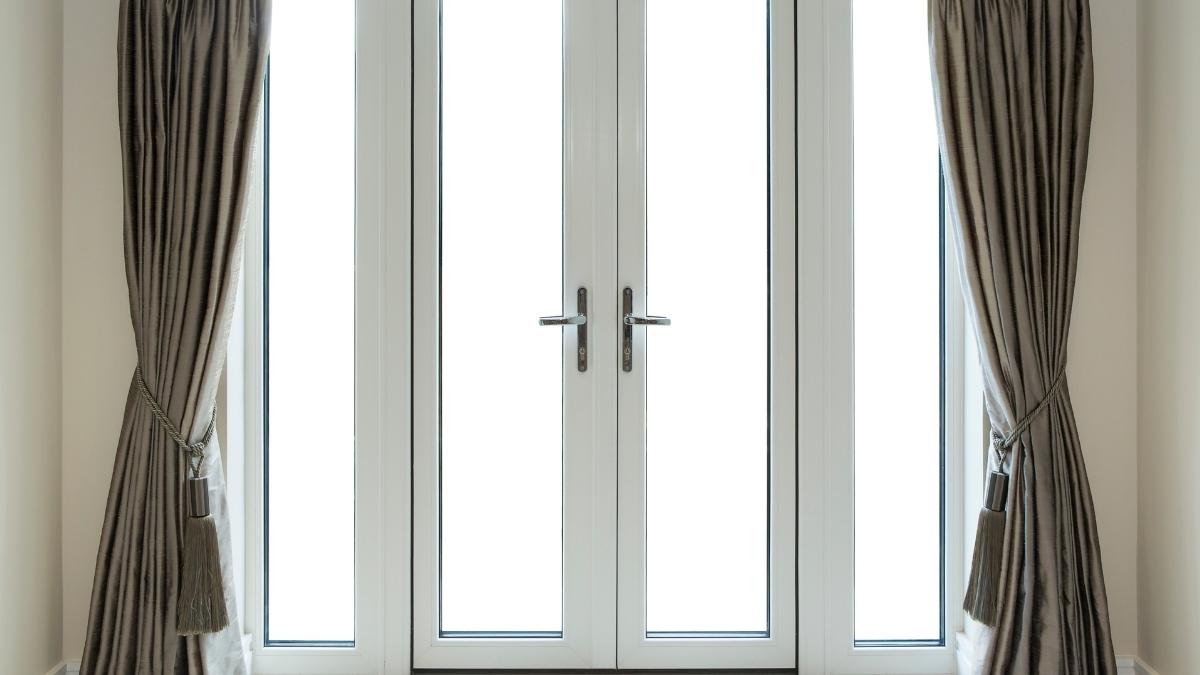 Een dubbele witte voordeur met glas en twee hoge zijlichten. Voor de deur hangt een grijs, geopend isolerend gordijn. 