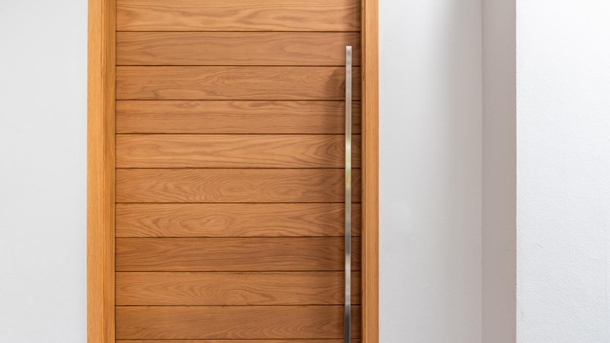 Een houten isolerende binnendeur met verticale planken en een lange, zilverkleurige deurgreep. De deur zit in een witte wand.