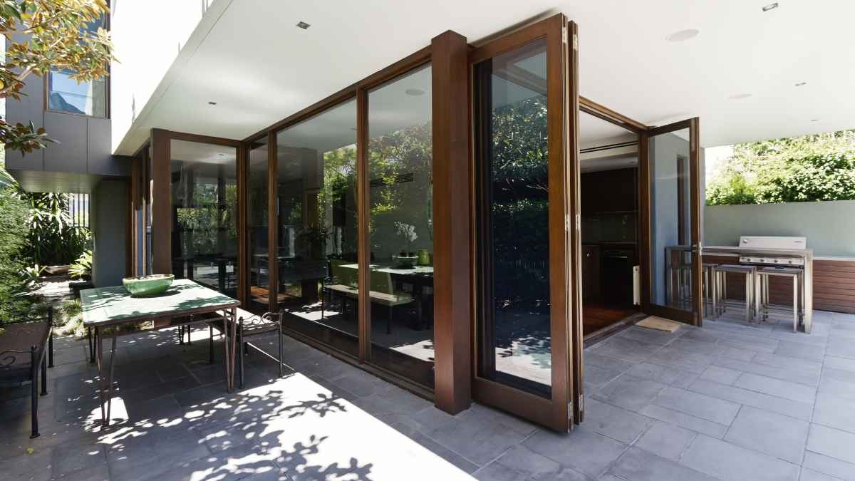 Een geopend vouwraam met profielen in houtlook. Het vouwraam verbindt een betegeld terras met een woonkamer.