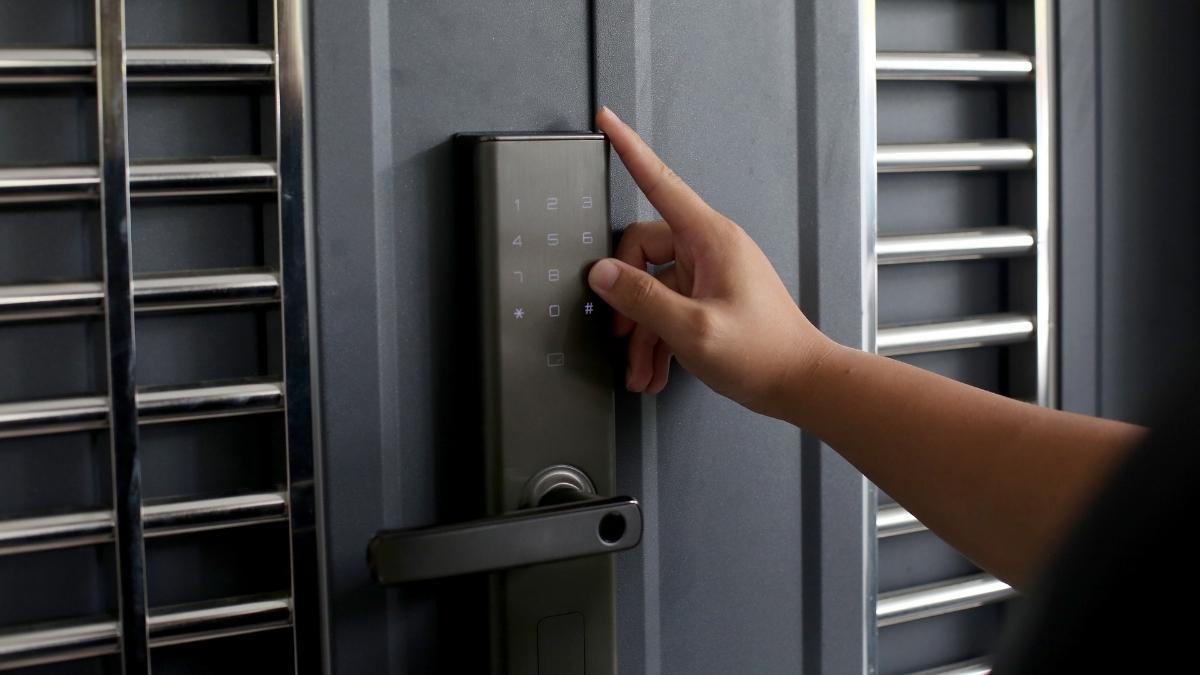 Een hand gebruikt het grijze klavier van een zwarte veiligheidsdeur.