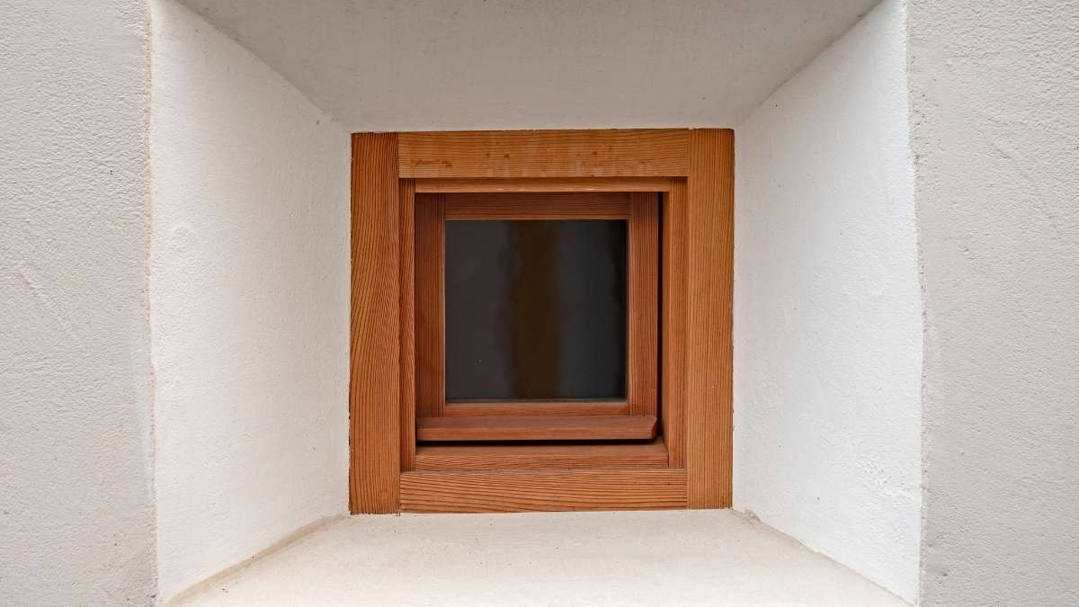 Een raam dat zeer diep in de muur ligt. Het raam heeft een houten raamkozijn met een warme, bruinrode tint. De dagkanten zijn bepleisterd in het wit. De onderste dagkant heeft een zeer zachte, wit-roze tint.