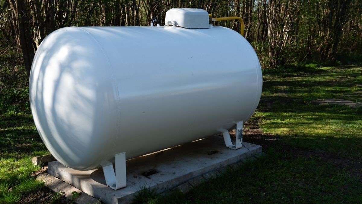 Witte bovengrondse gastank op een betonnen sokkel in de tuin met gele gasleiding, stabiele ondergrond bij gastank plaatsen